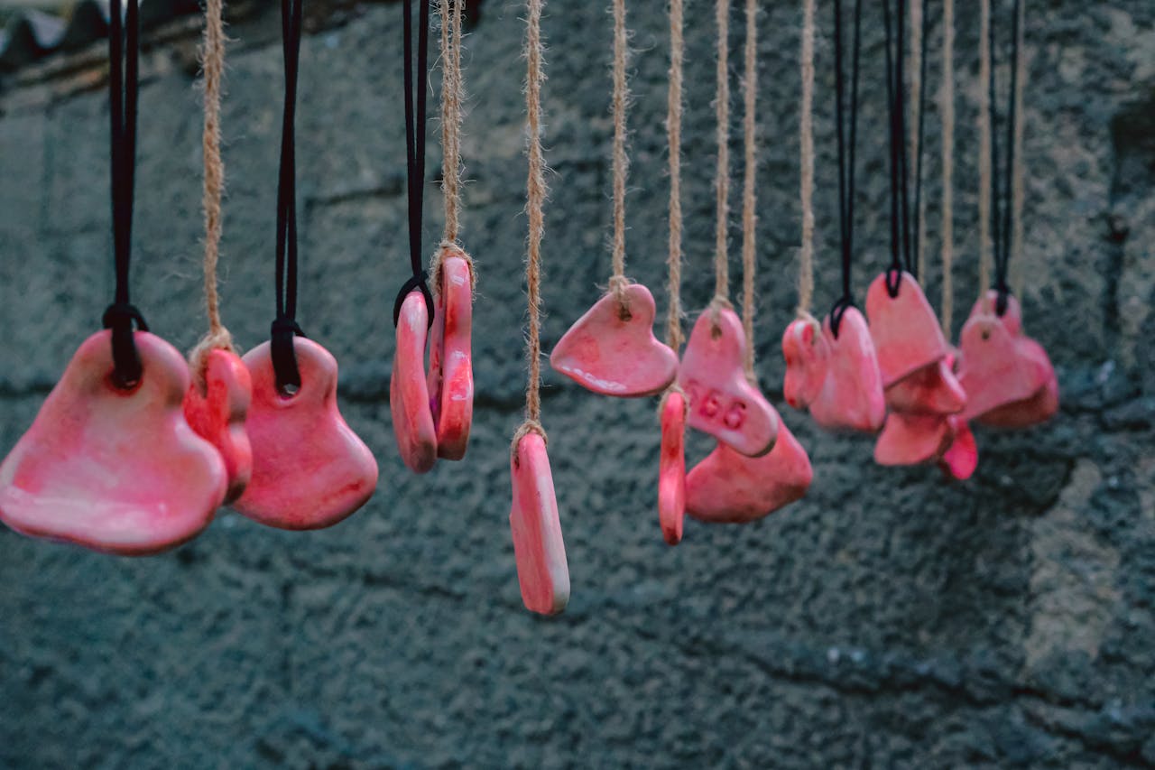 Vibrant heart-shaped ceramic pendants hanging against a textured wall, offering charm and simplicity.